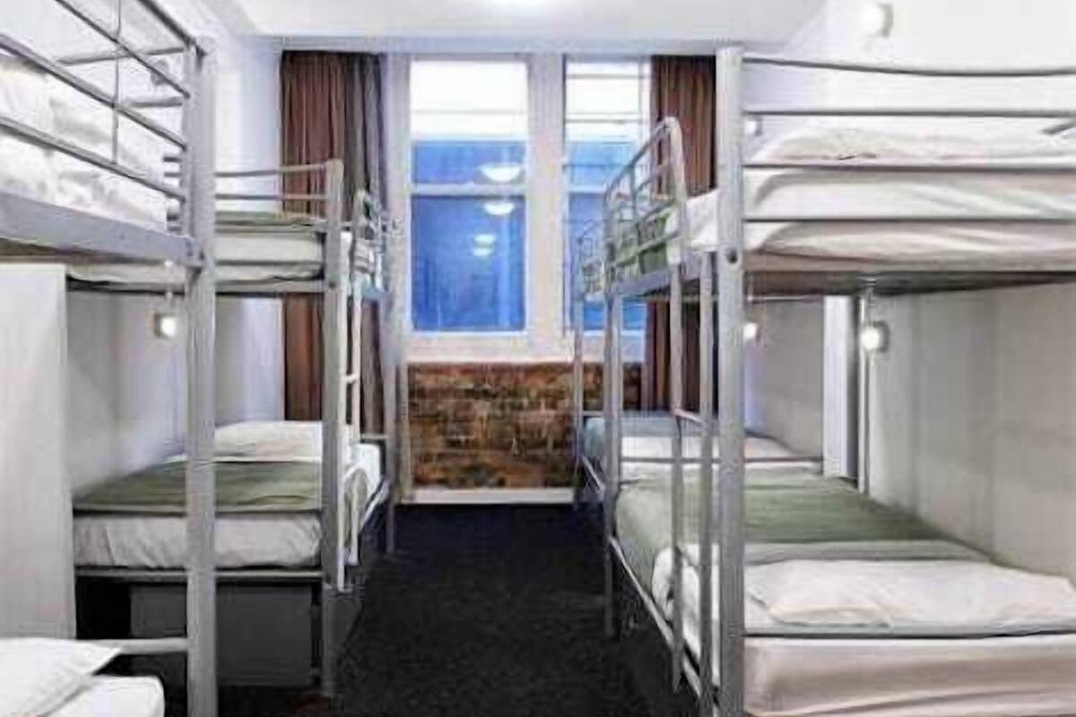 A room with bunk beds arranged in a row, a window with curtains, and a stone wall.