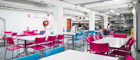 Una cafetería con mesas y sillas, un extintor y una señal de salida visible.