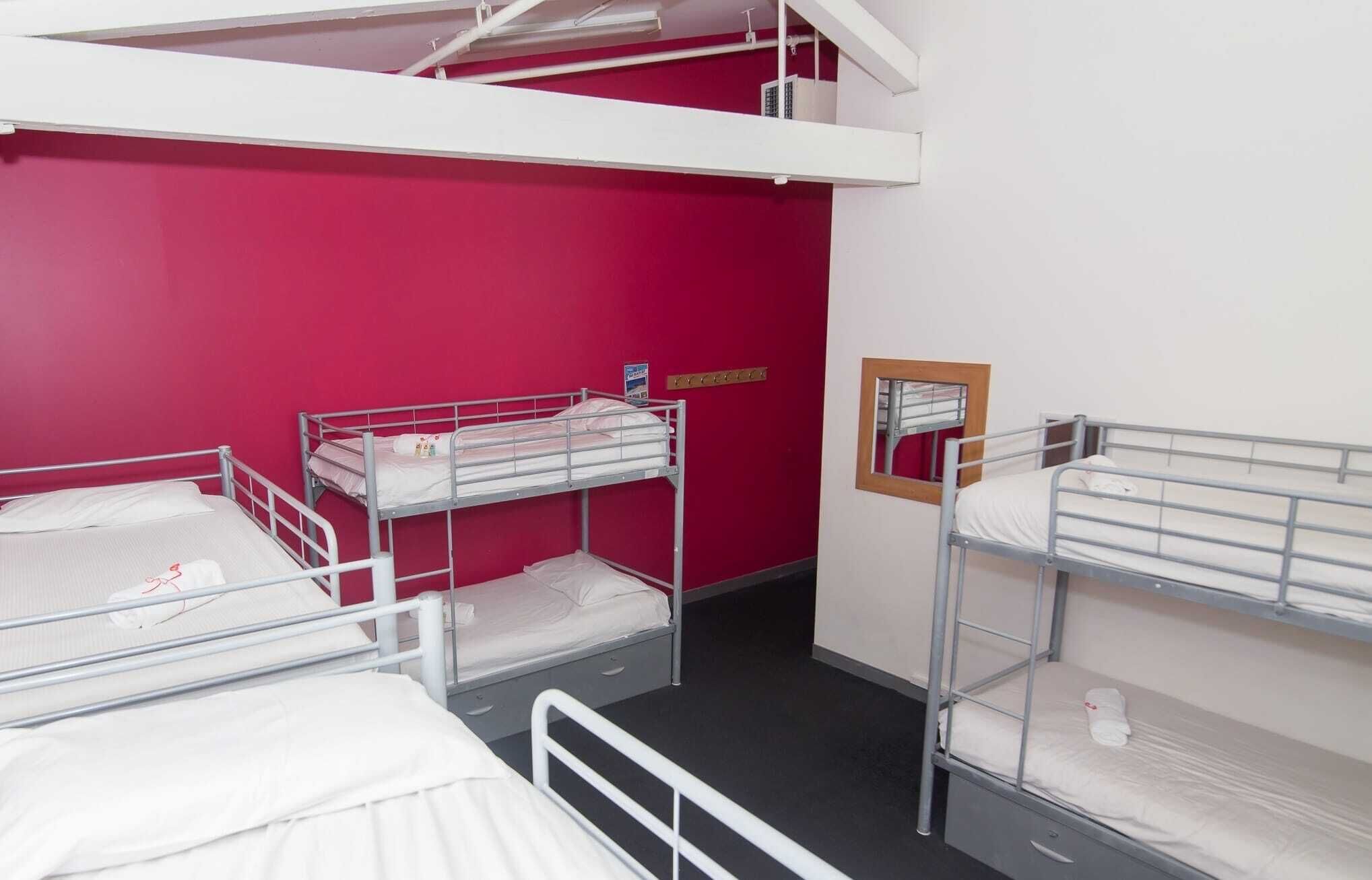 Une chambre de dortoir avec des lits superposés, un mur rouge et un petit miroir accroché au mur.