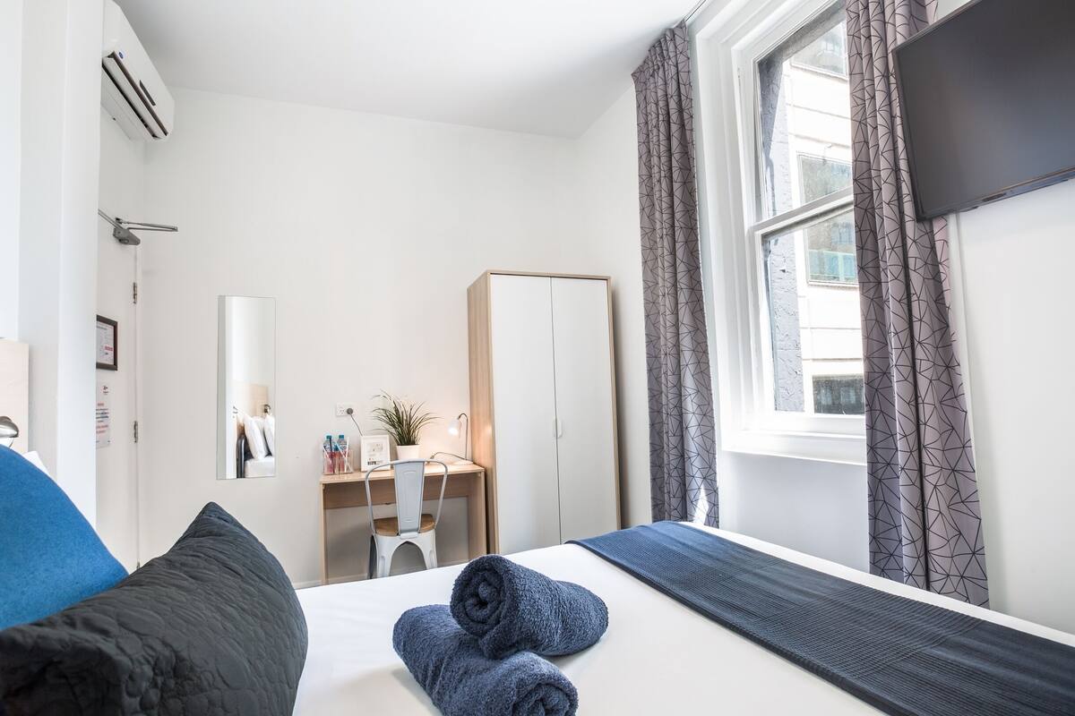 A hotel room with a bed, a desk, a chair, a wardrobe, and a window with curtains.