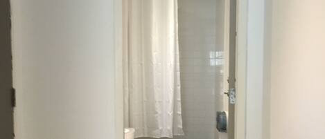 Un couloir étroit menant à une salle de bain équipée de toilettes, d’une douche et d’un rideau.