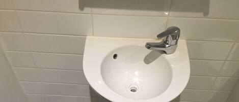A bathroom sink with a chrome faucet, a plastic trash bag on the floor, and a toilet brush.