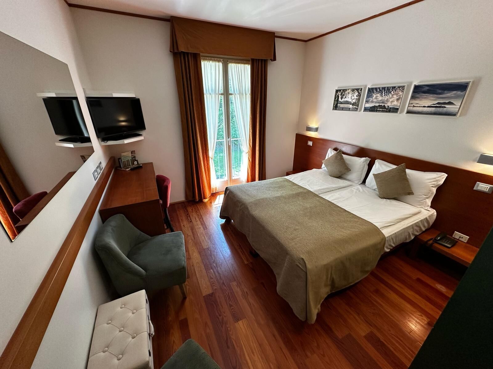 Habitación de hotel con cama, escritorio, silla, televisor y ventana con cortinas.