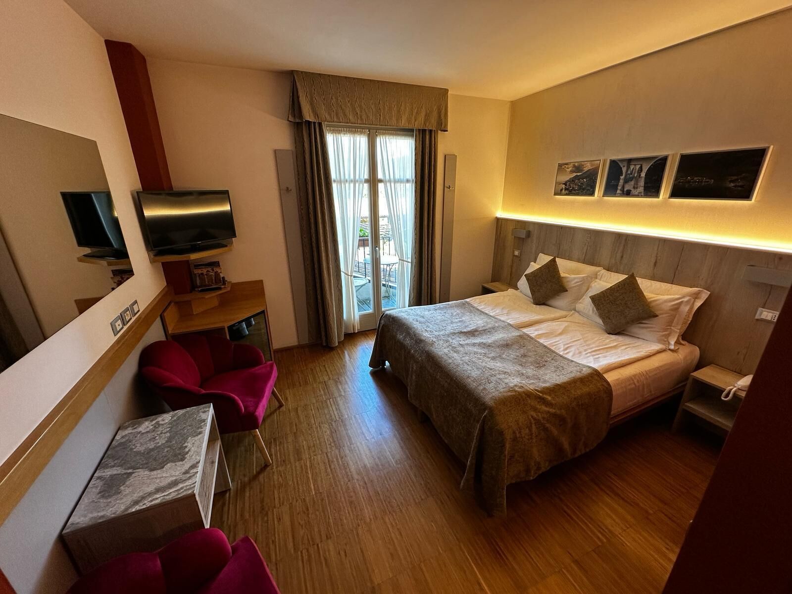 A hotel room with a bed, a desk with a chair, a television, and a window with curtains.