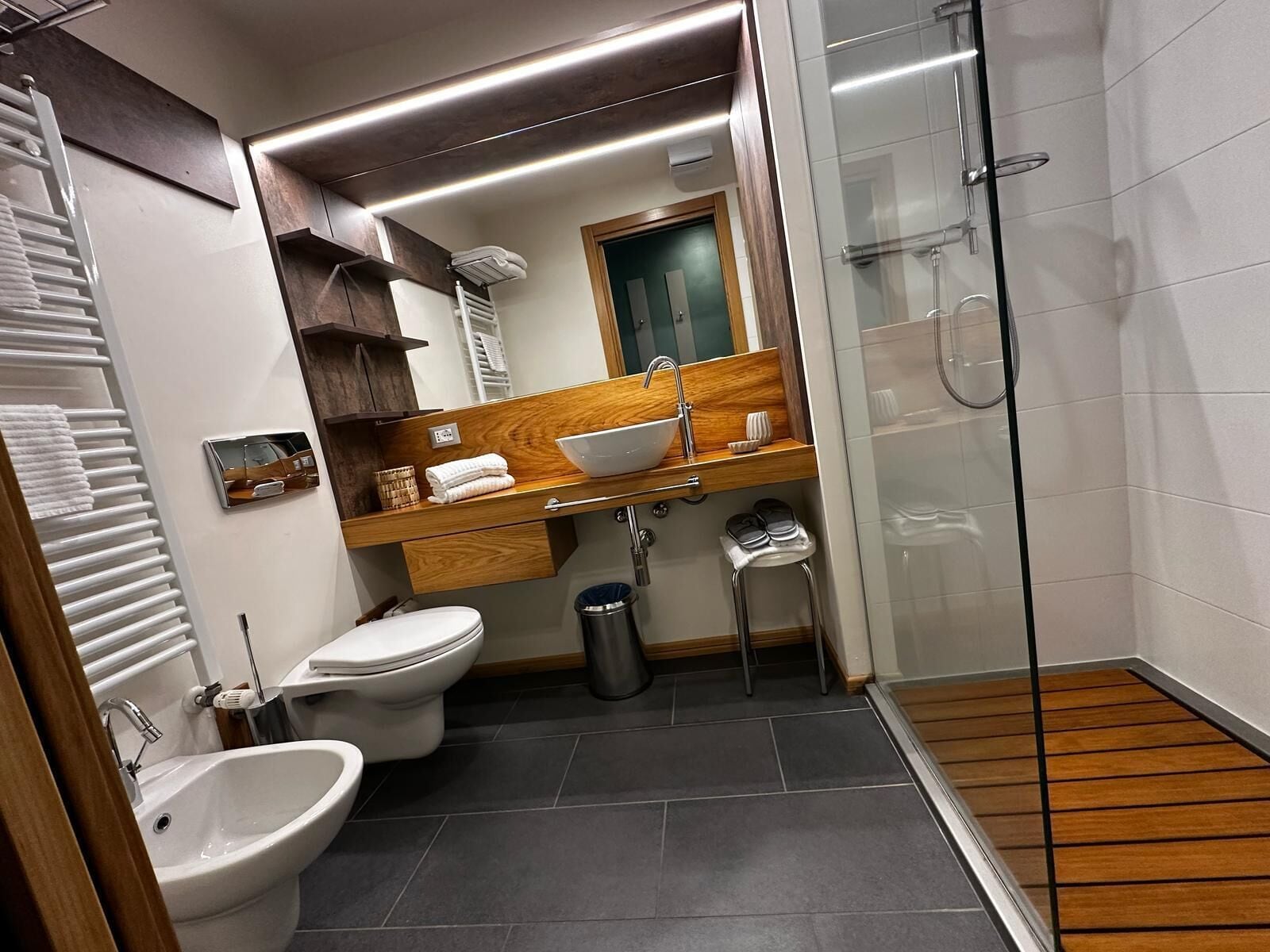 A modern bathroom with a wooden vanity, a glass shower enclosure, a bidet, and a toilet.