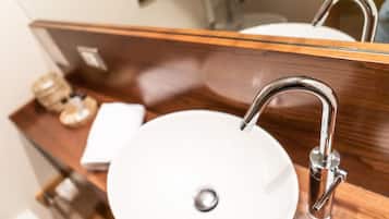 A bathroom sink with a chrome faucet and a round basin, a wooden countertop, and a mirror reflecting the sink and faucet.
