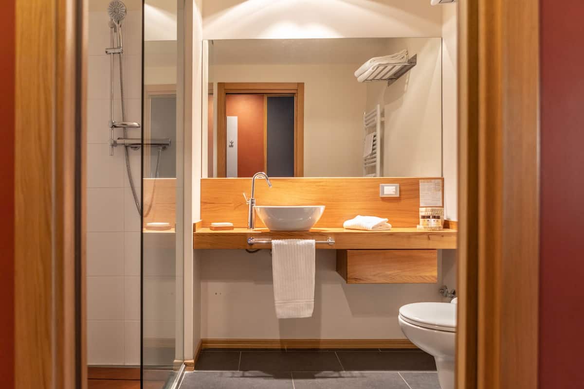 Un baño moderno con ducha acristalada, tocador de madera con lavabo y un inodoro.