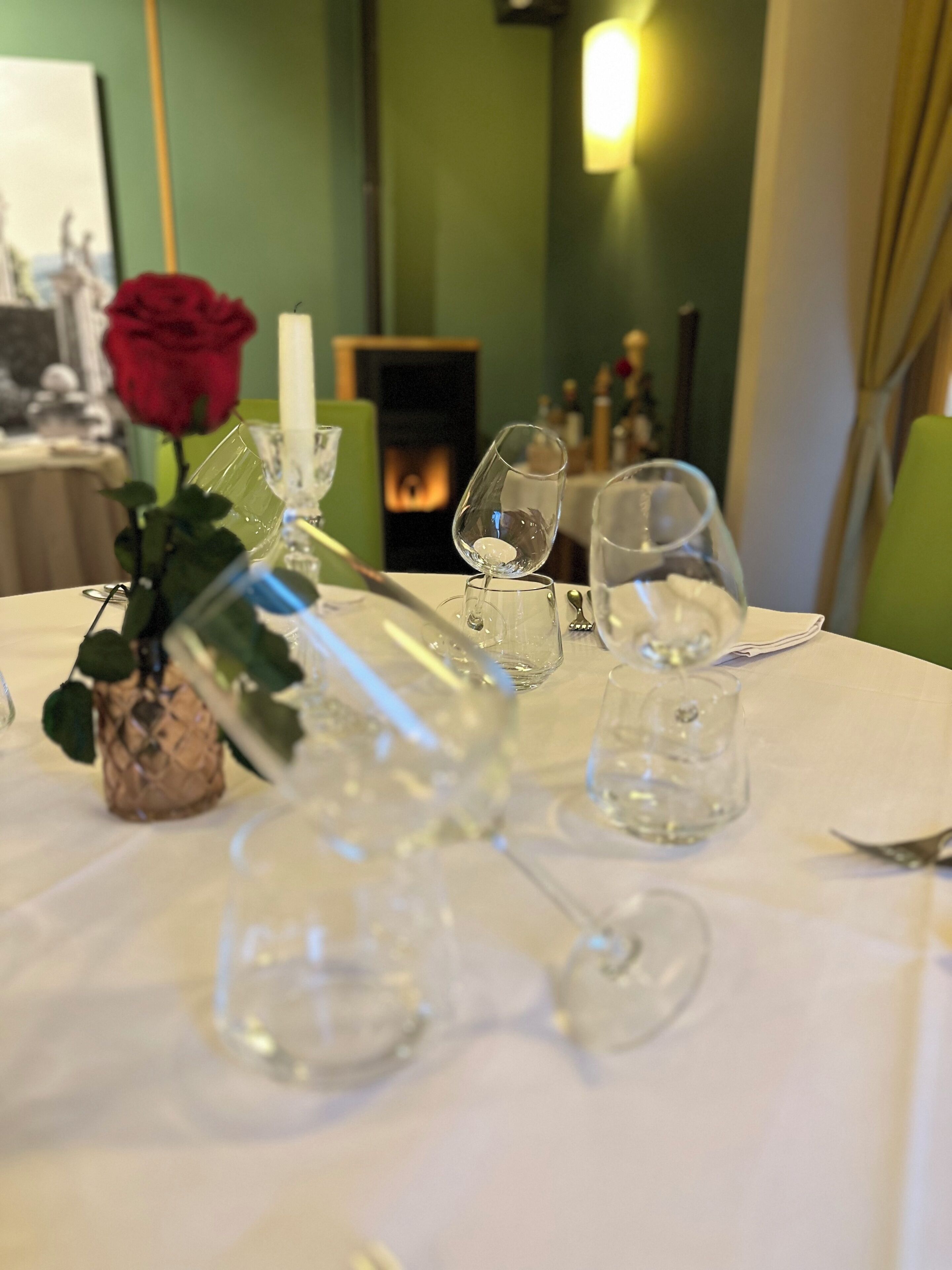 A dining table set with wine glasses and a candle, with a rose and a decorative vase in the foreground.