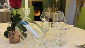 A dining table set with wine glasses and a candle, with a rose and a decorative vase in the foreground.