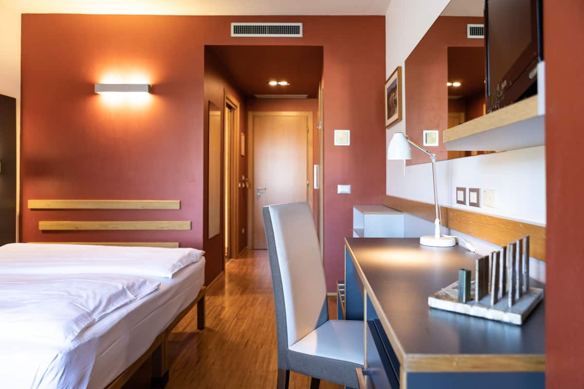 Habitación de hotel con cama, escritorio, silla, lámpara de escritorio y espejo.
