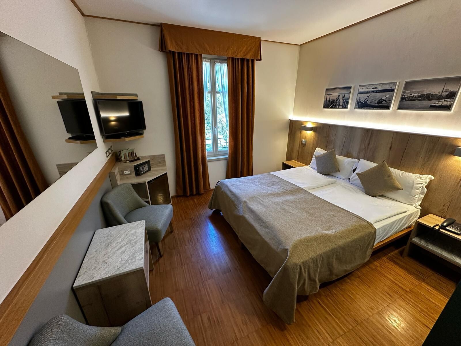 Ein Hotelzimmer mit Bett, Nachttischen, Schreibtisch, Stuhl, Fernseher und einem Fenster mit Vorhängen.