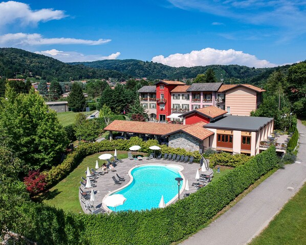 A hotel with a swimming pool, surrounded by lush greenery and a mountainous backdrop. - Hotel Cortese (Armeno)