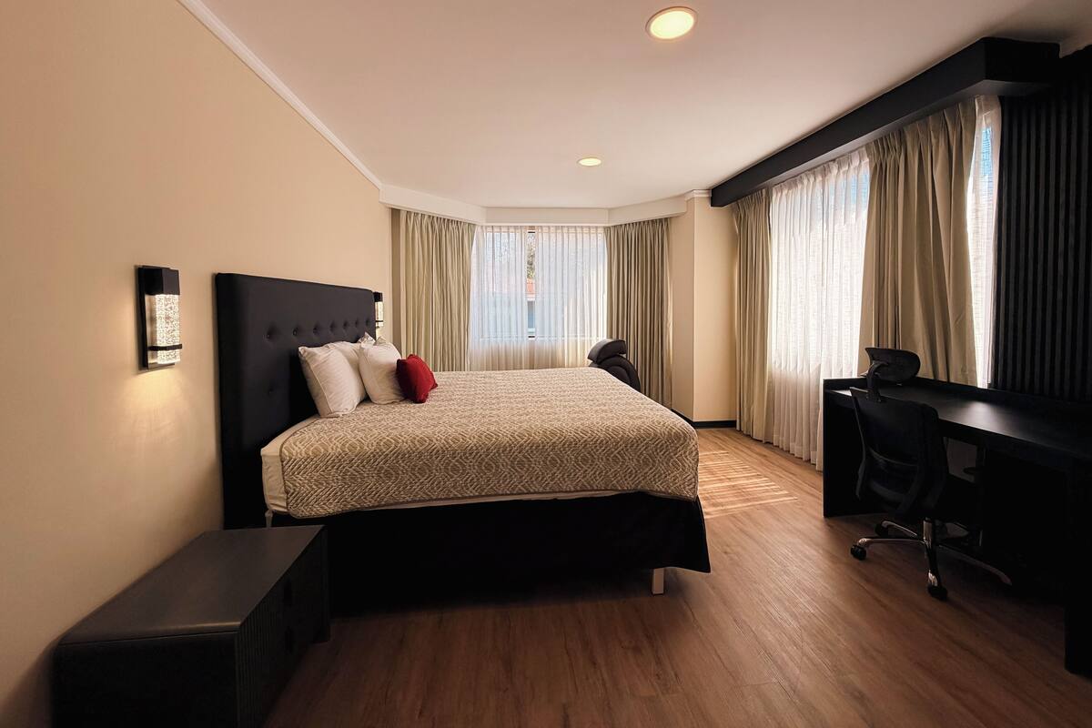 A modern hotel room with a large bed, a desk, and a chair.