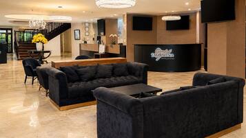 A hotel lobby with a reception desk, sofas, a staircase, and a chandelier.
