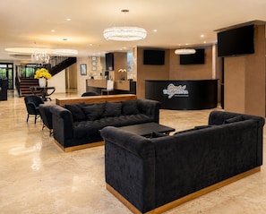 A hotel lobby with a reception desk, sofas, a staircase, and a chandelier. - Taormina Hotel and Casino  (San José)