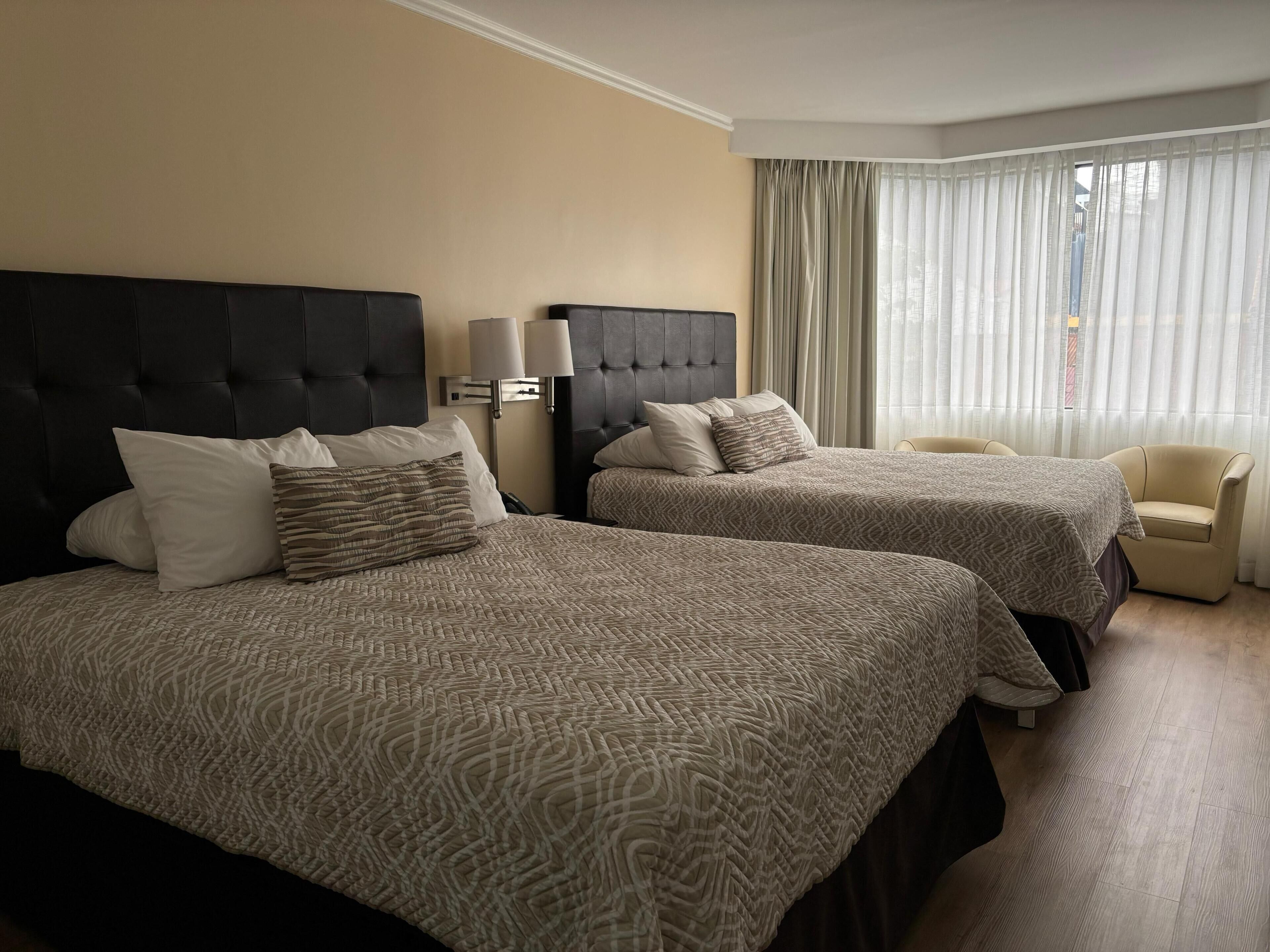 A hotel room with two beds, a chair, and a large window with curtains.