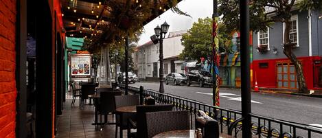 An outdoor cafe with tables and chairs, a street view, and a building with a red facade.