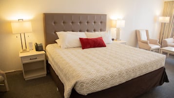 Una habitación de hotel con una cama grande, dos mesitas de noche, una lámpara y una silla.