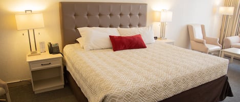 Una habitación de hotel con una cama grande, dos mesitas de noche, una lámpara y una silla.
