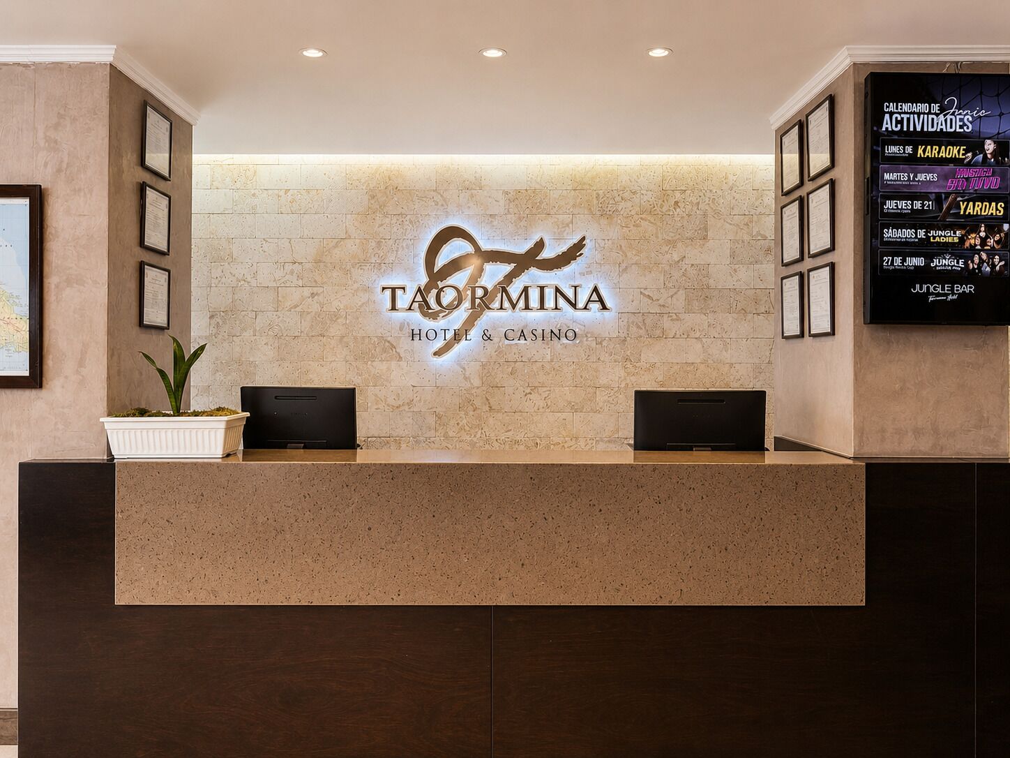 A reception desk with a logo for Taormina Hotel & Casino, framed certificates, and a wall-mounted calendar listing events.
