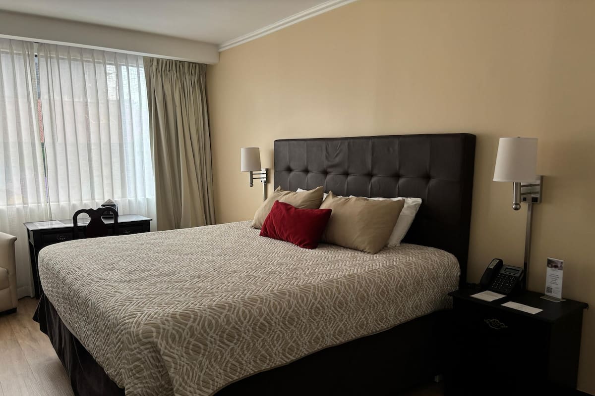 A hotel room with a large bed, two bedside tables, a desk, and a window with curtains.