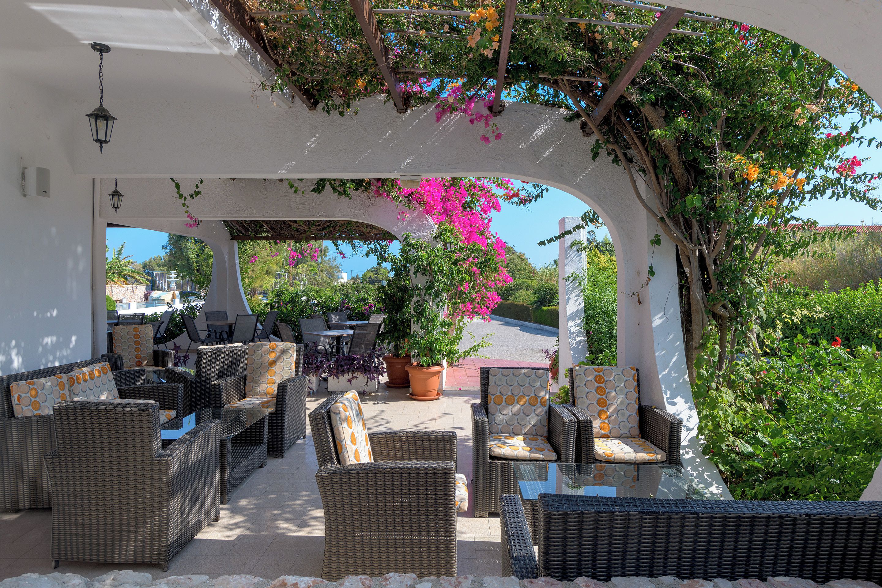 An outdoor seating area with wicker furniture and a pergola covered with flowering vines.