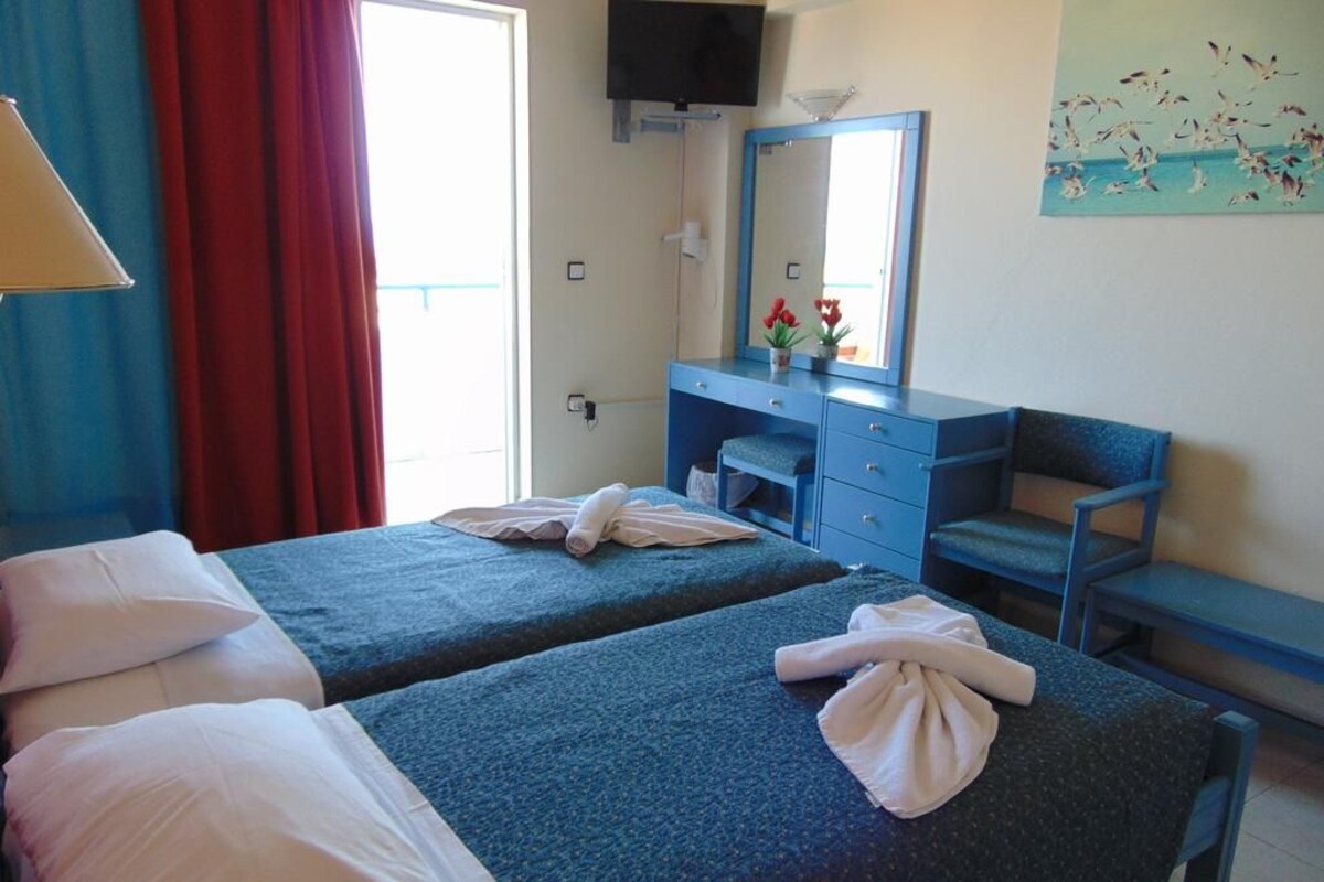 A hotel room with two beds, a desk, a chair, a television, and a painting on the wall.