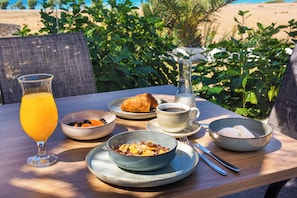A breakfast table with a glass of orange juice, a bowl of cereal, a croissant, a cup of coffee, and a teapot. - Nirvana Beach (Rhodes)