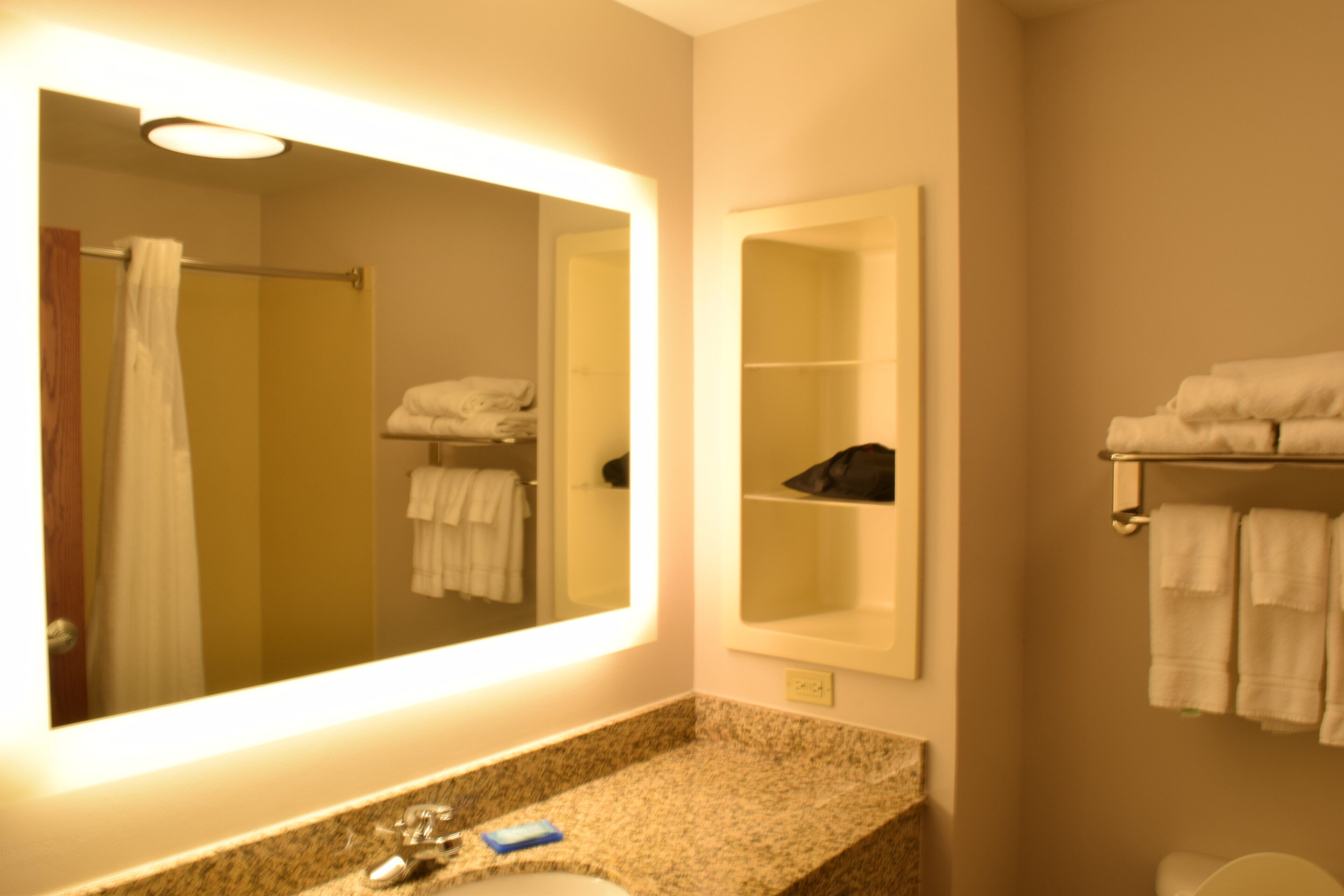 A bathroom with a large mirror, a sink with a faucet, a towel rack, and a shelf with towels.