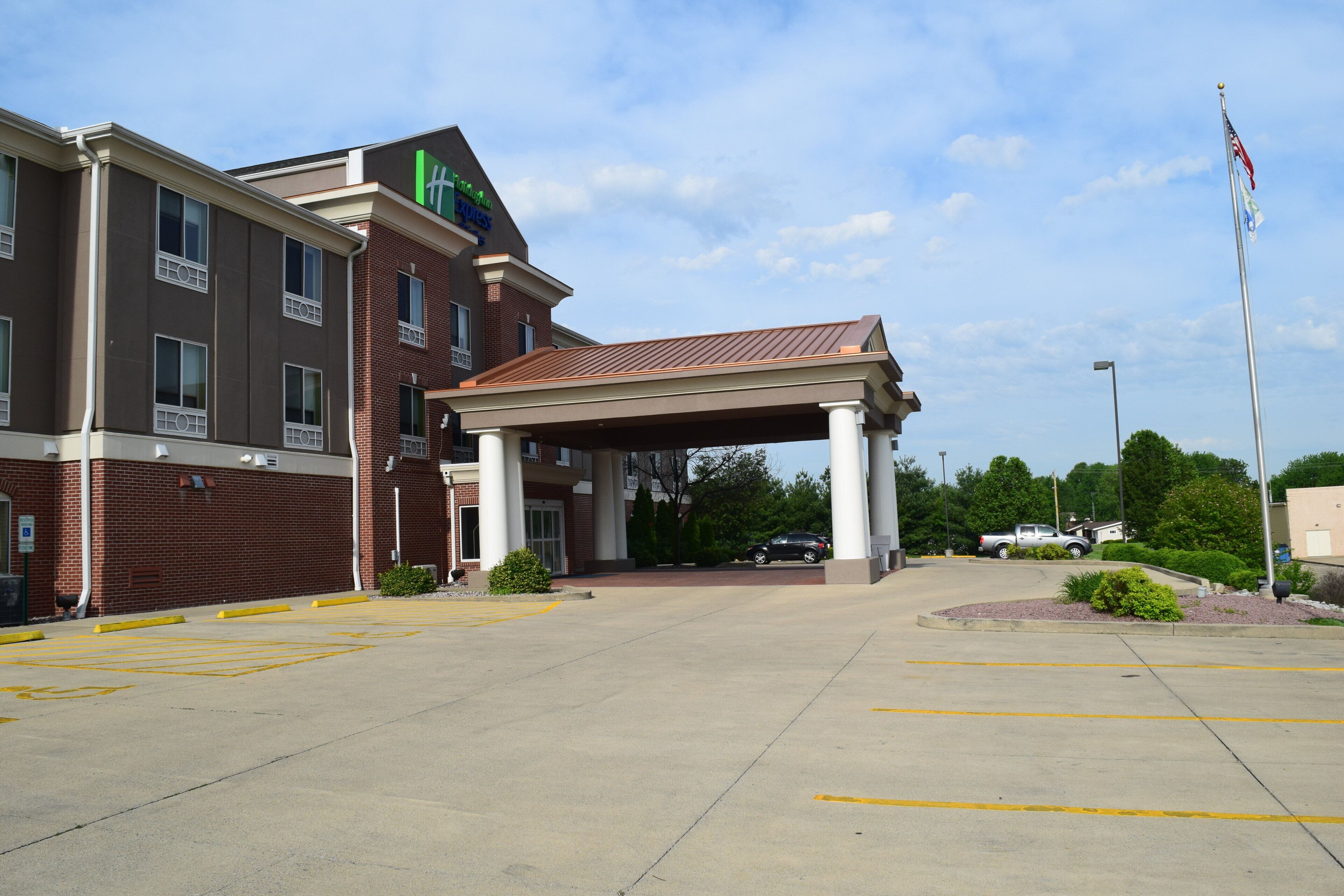 A hotel entrance with a covered parking area, a flagpole with an American flag, and a clear sky.