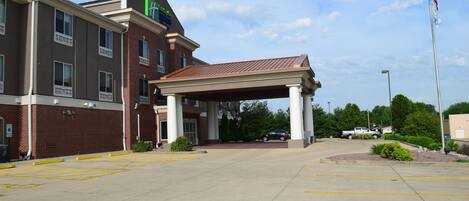 A hotel entrance with a covered parking area, a flagpole with an American flag, and a clear sky.