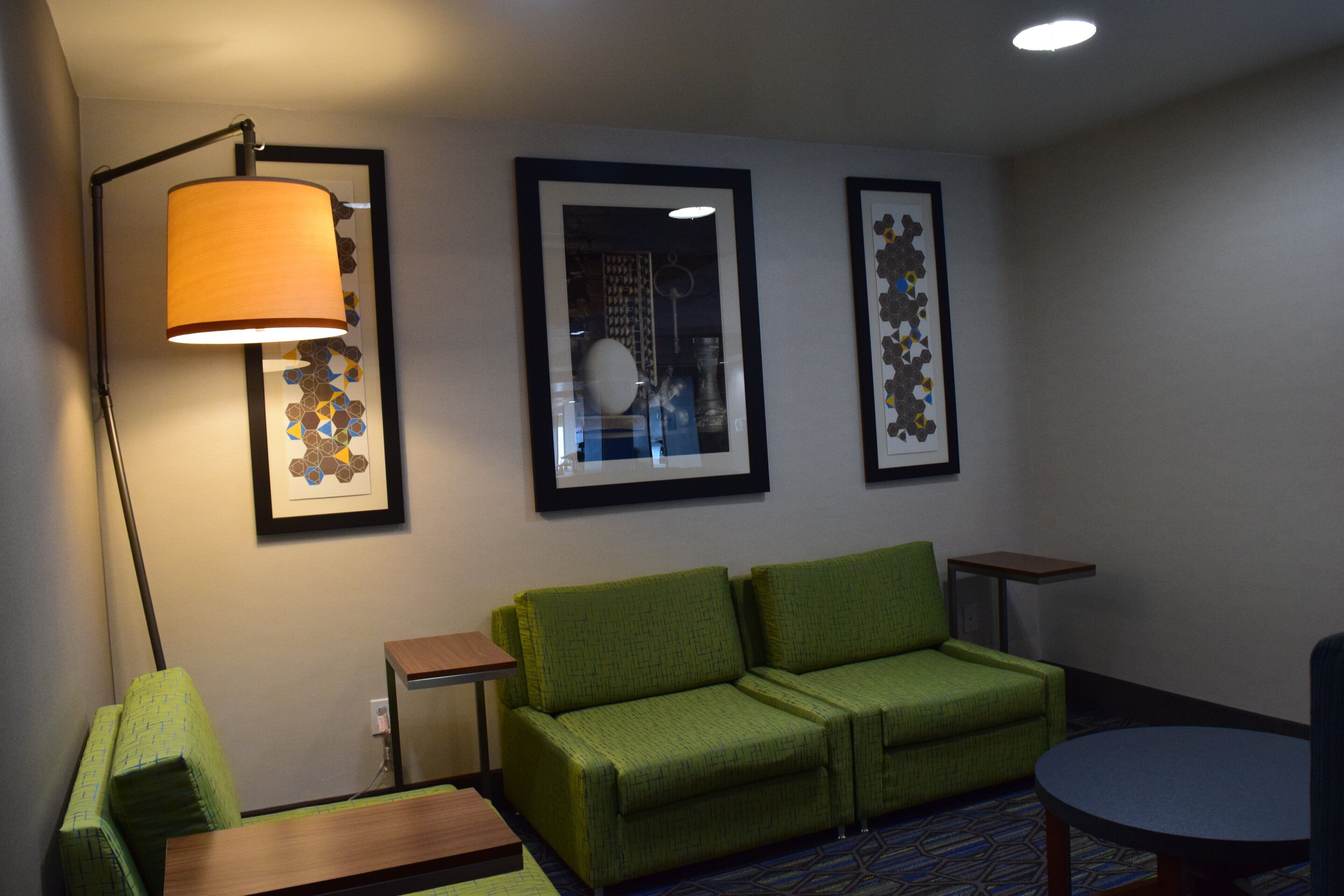 Una habitación de hotel con un sofá verde, una lámpara de pie y tres cuadros en la pared.