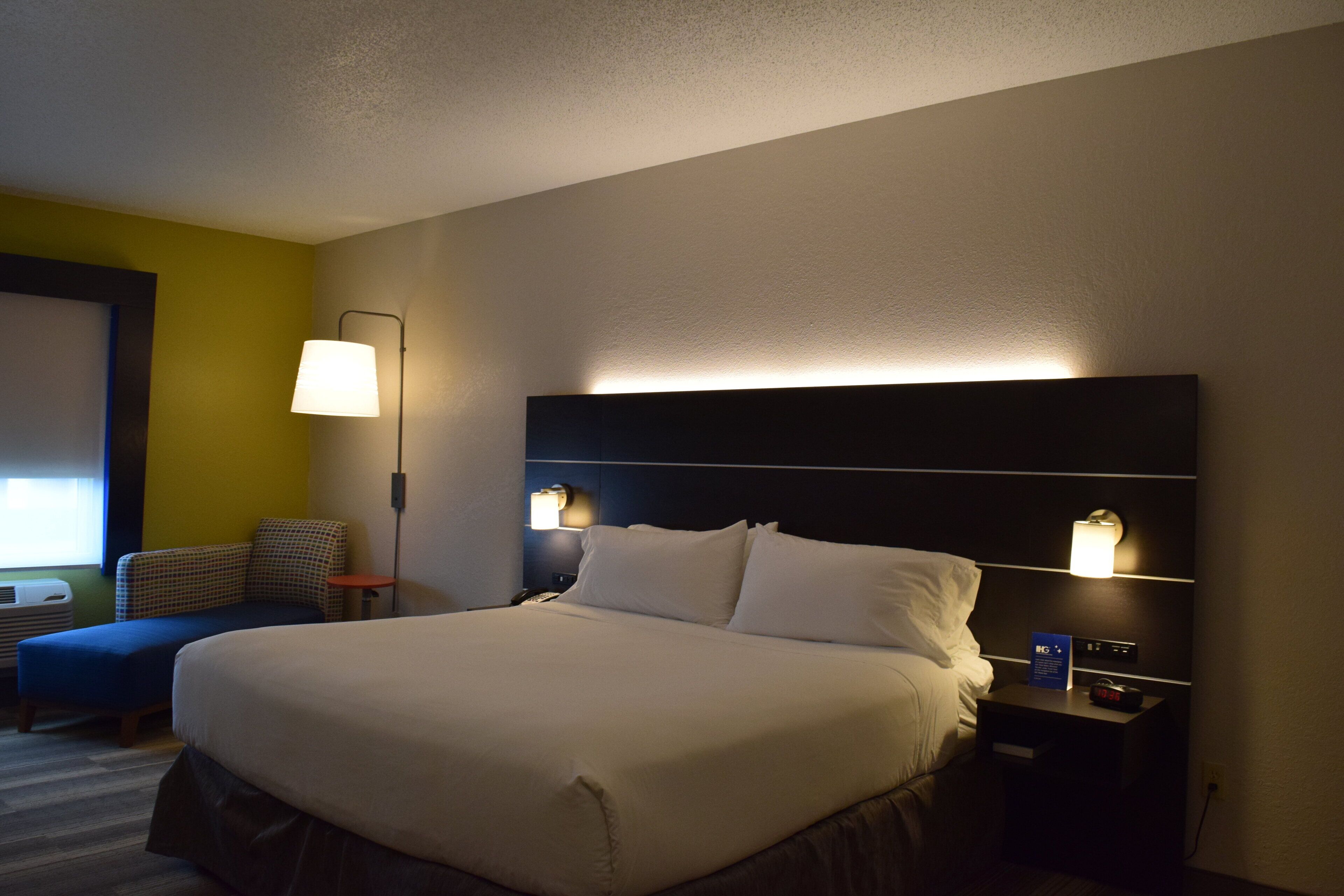Una habitación de hotel con una cama grande, mesitas de noche, una lámpara y una silla.