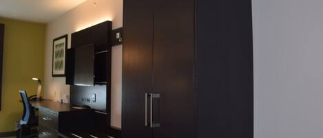 A modern room with a dark wooden desk, a chair, a large mirror, and a wardrobe.