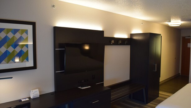 Habitación de hotel con una televisión de pantalla plana grande, un escritorio con cajones, un banco y un armario.