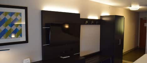Una habitación de hotel con una cama, un escritorio con ordenador, un televisor y un armario.