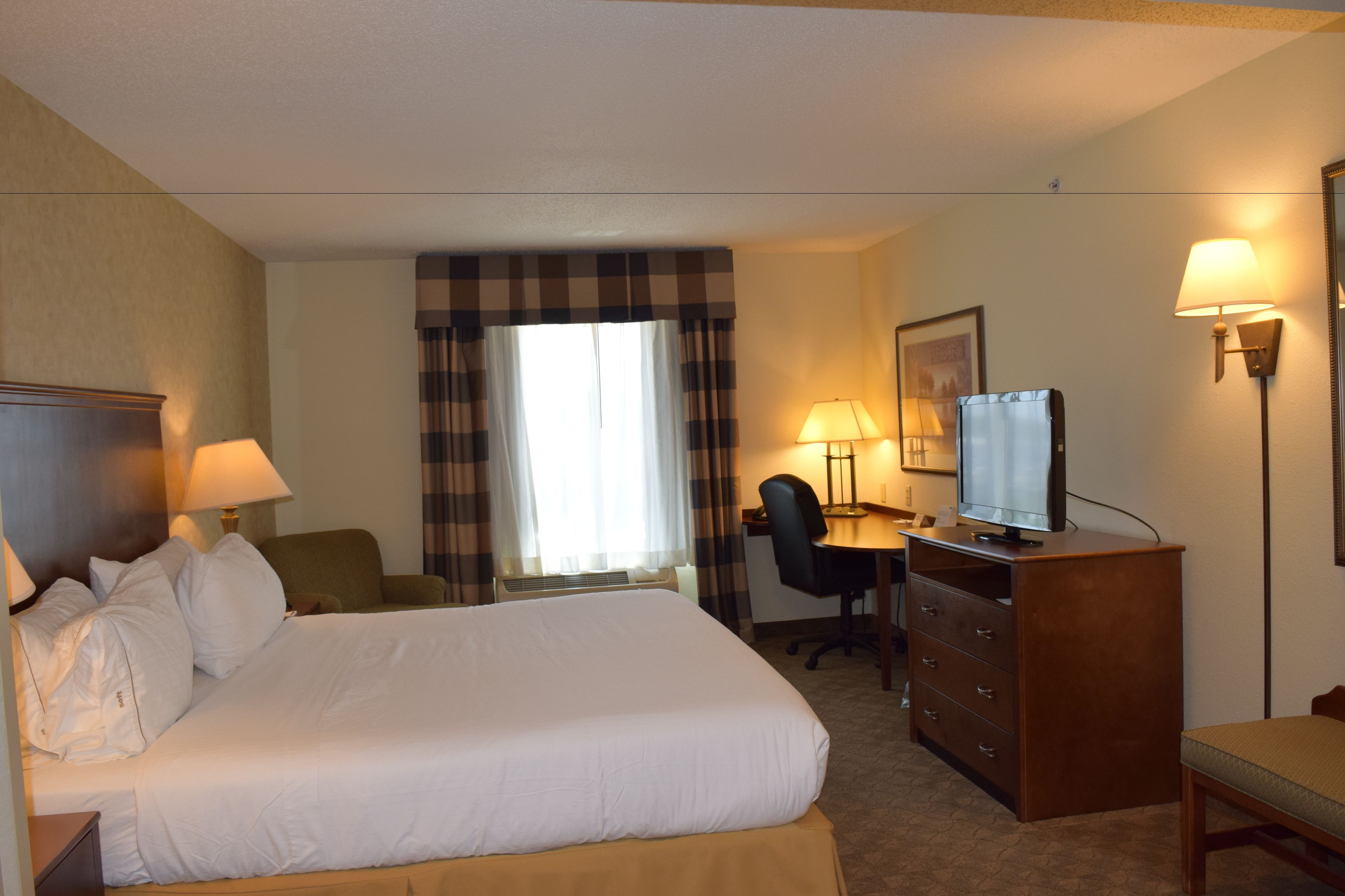 A hotel room with a large bed, a desk with a chair, a television, and two lamps.