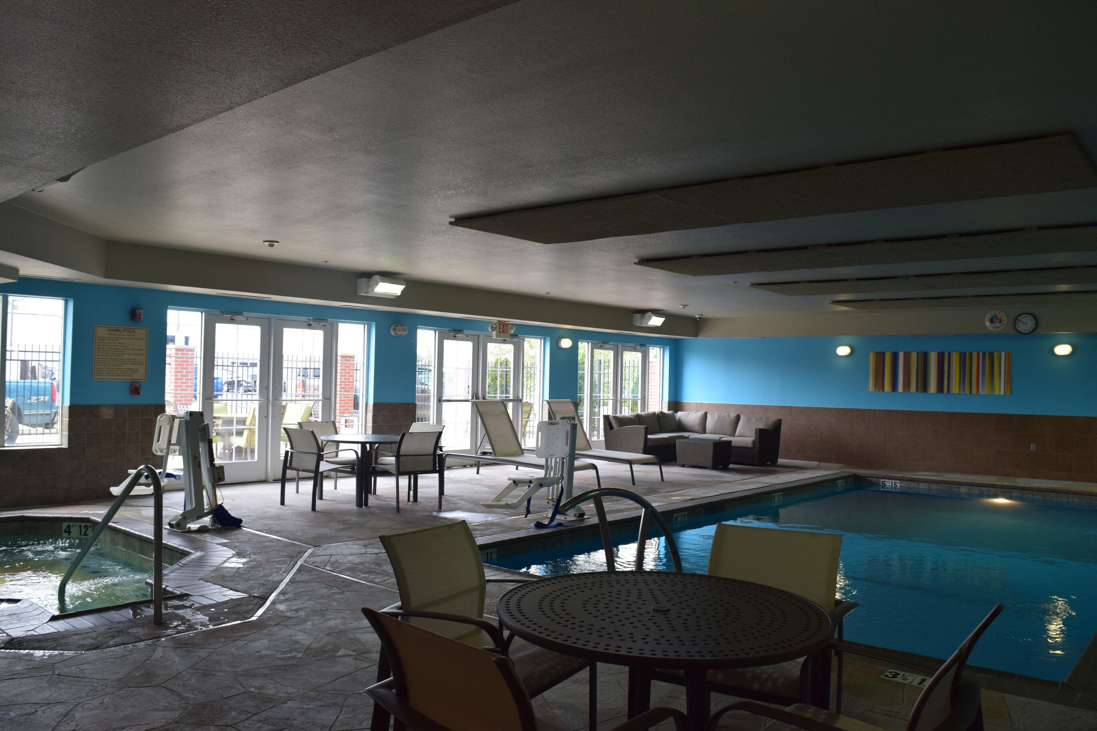 An indoor swimming pool area with lounge chairs, a pool table, and a clear view of the outside through large windows.