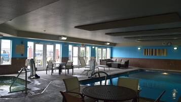 An indoor swimming pool area with lounge chairs, a pool table, and a clear view of the outside through large windows.