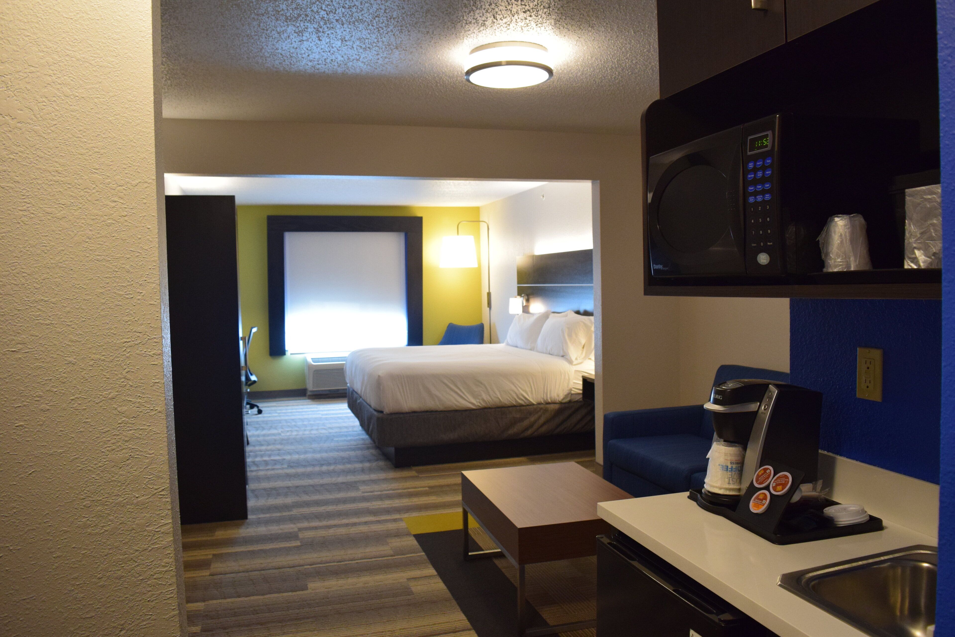 Una habitación de hotel con cama, escritorio, microondas, cafetera y lavamanos.