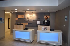 A hotel reception desk with a digital display, a desk phone, and a computer. There is a sign indicating the hotel's name and services. - Holiday Inn Express Hotel & Suites Sparta by IHG (Sparta)