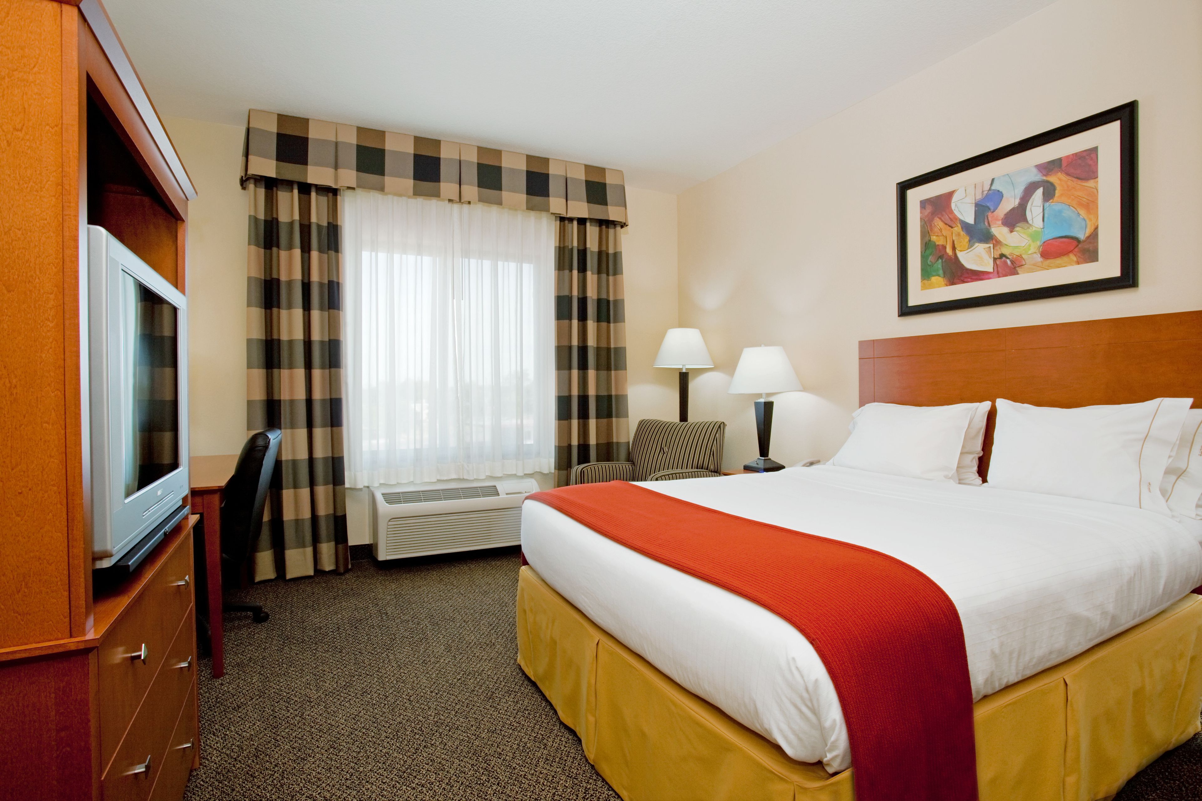A hotel room with a bed, a television, a desk, a chair, a lamp, and a painting on the wall.