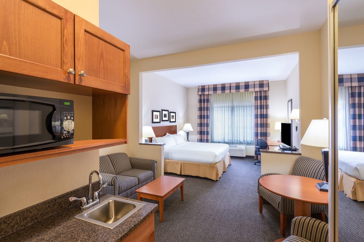 A hotel room with a kitchenette, a bed, a desk, a chair, and a sofa.