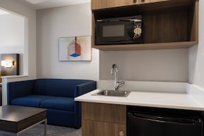 A compact kitchenette with a microwave, a sink, and a dishwasher. There is a blue sofa and a small table in the room. - Holiday Inn Express Vernal-Dinosaurland by IHG (Vernal)