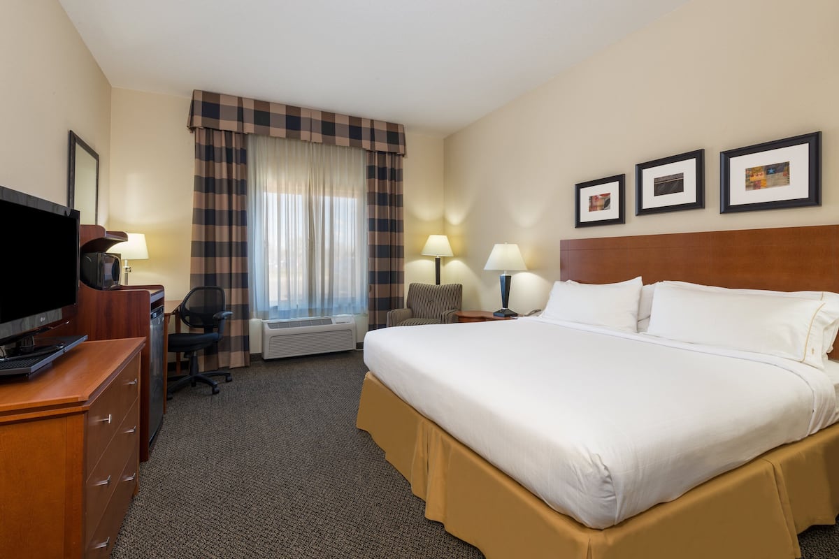 A hotel room with a large bed, a desk with a computer, a television, and a window with curtains.