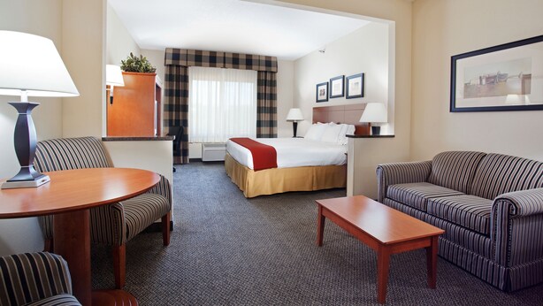 Ein Hotelzimmer mit einem Bett, zwei gestreiften Sofas, einem Holztisch und einem Schreibtisch mit einer Lampe.