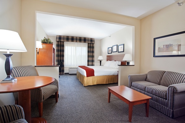 A hotel room with a bed, two striped sofas, a wooden table, and a desk with a lamp.