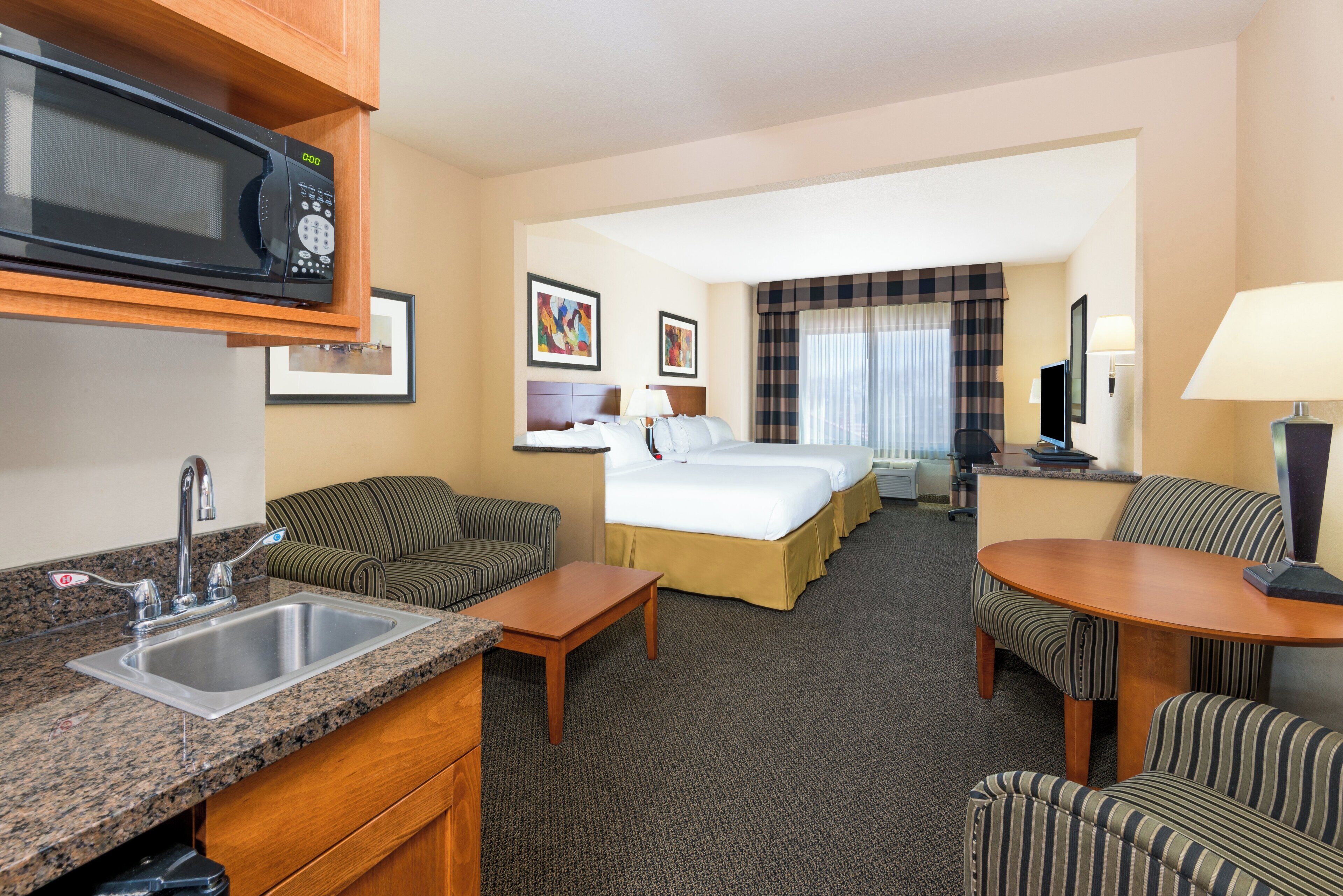 A hotel room with a kitchenette, a bed, a sofa, a dining table, and a TV.