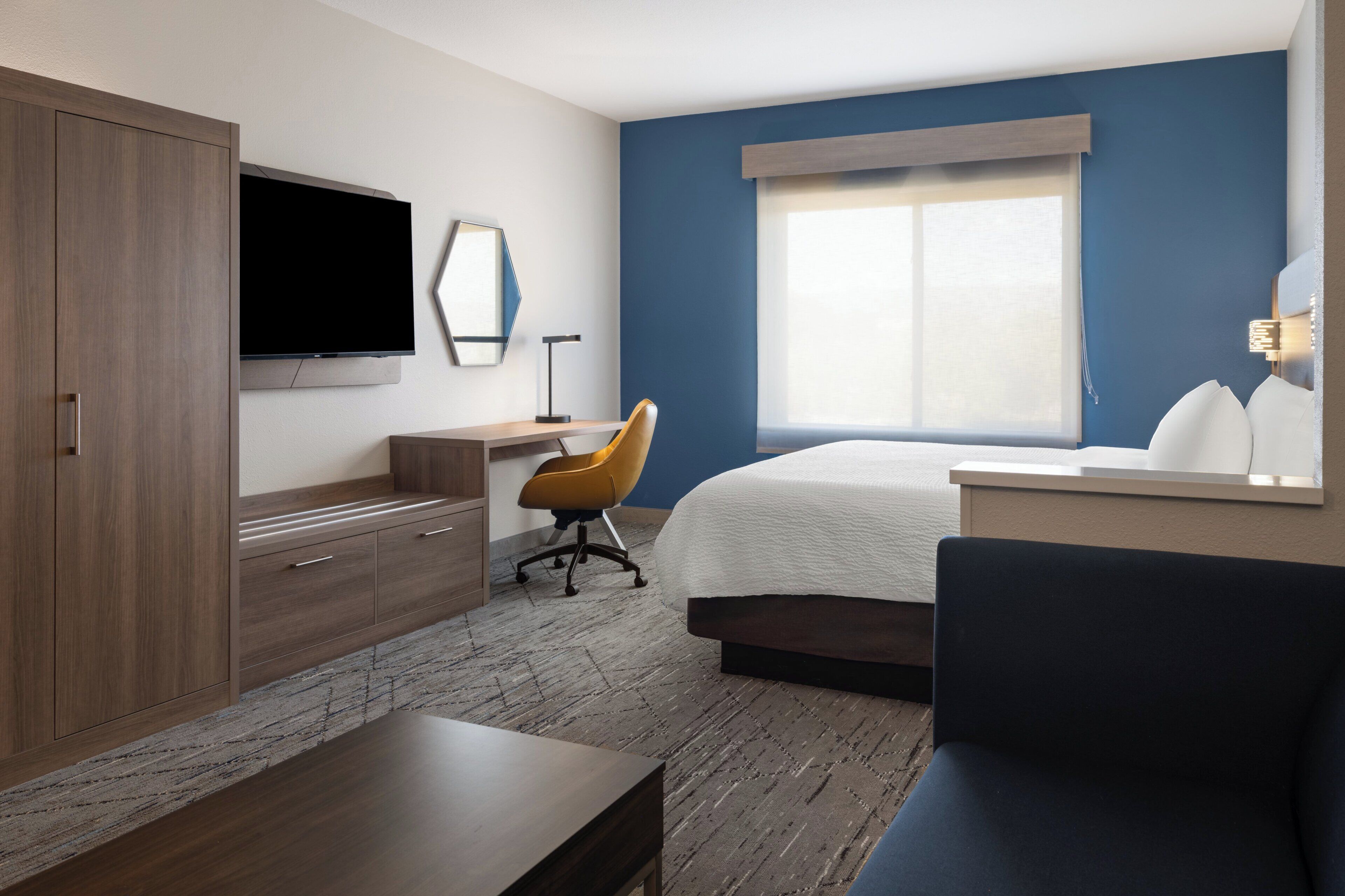 Une chambre d’hôtel avec un lit, un bureau, une chaise, une télévision et une fenêtre.