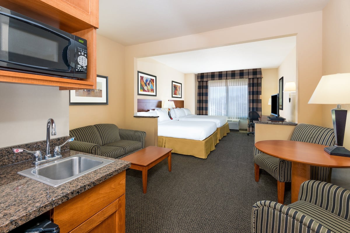 A hotel room with a kitchenette, a bed, a sofa, a dining table, and a TV.